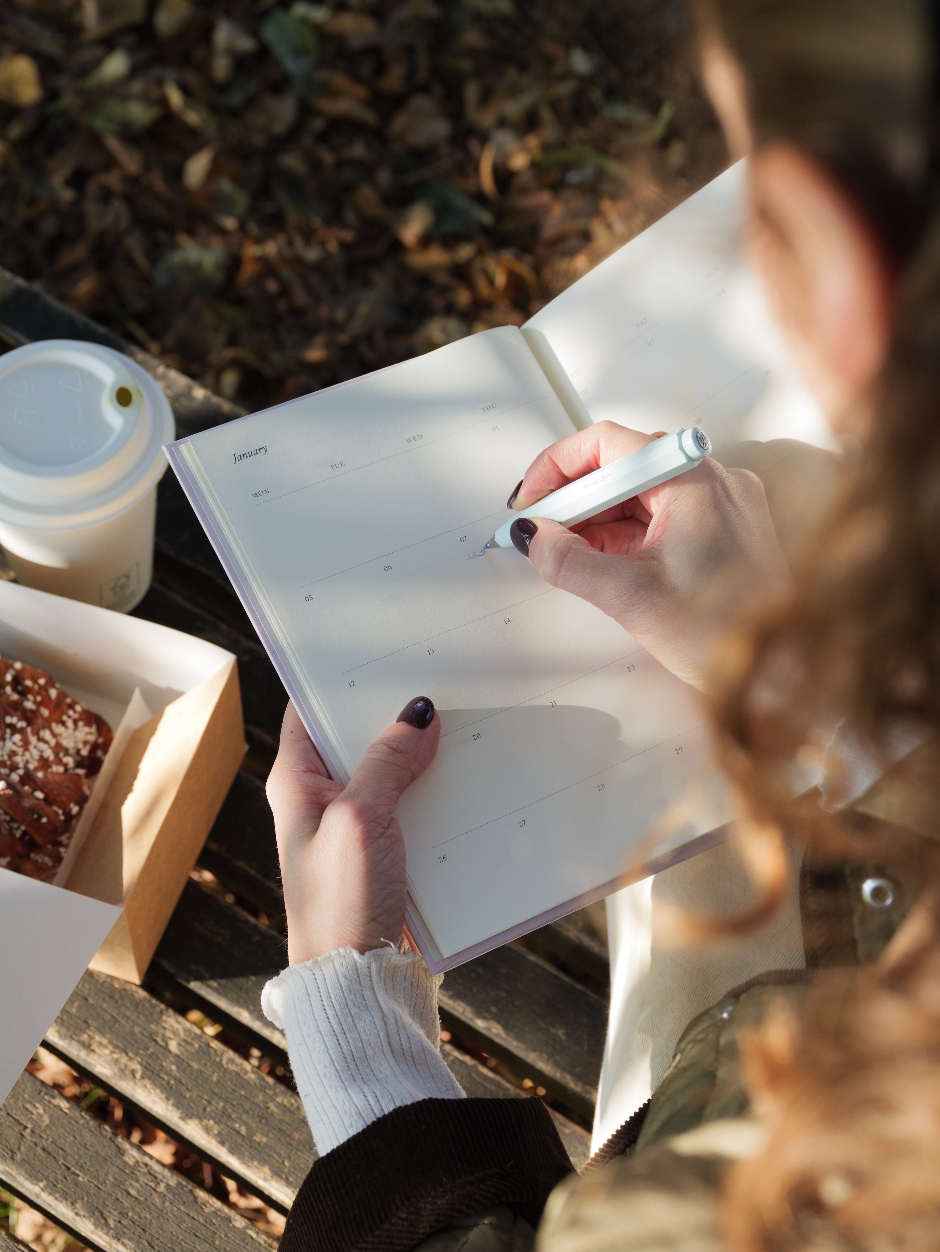 Widok z nad ramienia kobiety piszącej w różowym kalendarzu Jaśnie Plan na rok 2026